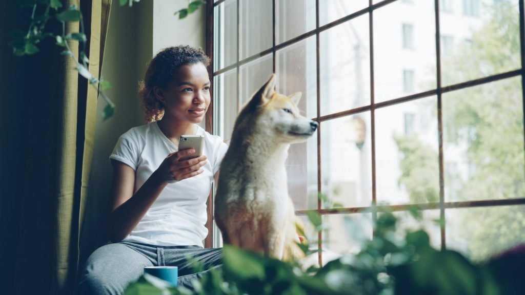 Mulher e cão olhando pela janela juntos